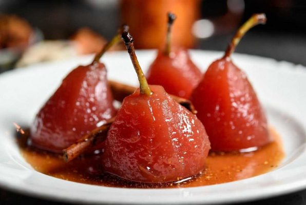 Quatre poires pochées au vin rouge dans une assiette