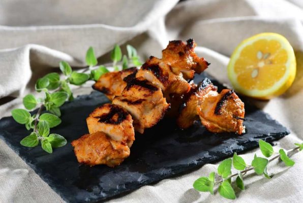 Deux pinchitos morunos bien grillés, sur une ardoise, à côté des brins d'origan et un demi citron
