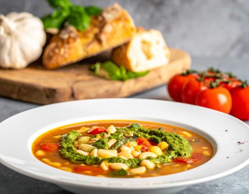 Assiette de soupe au pistou, derrière, de l'ail, du basilic, du pain et une grappe de tomates