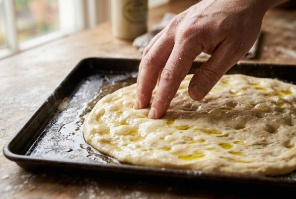 Façonnage de la schiacciata toscane : doigts qui creusent les empreintes caractéristiques sur la pâte huilée. Pain plat italien moelleux et parfumé à l’huile d’olive.